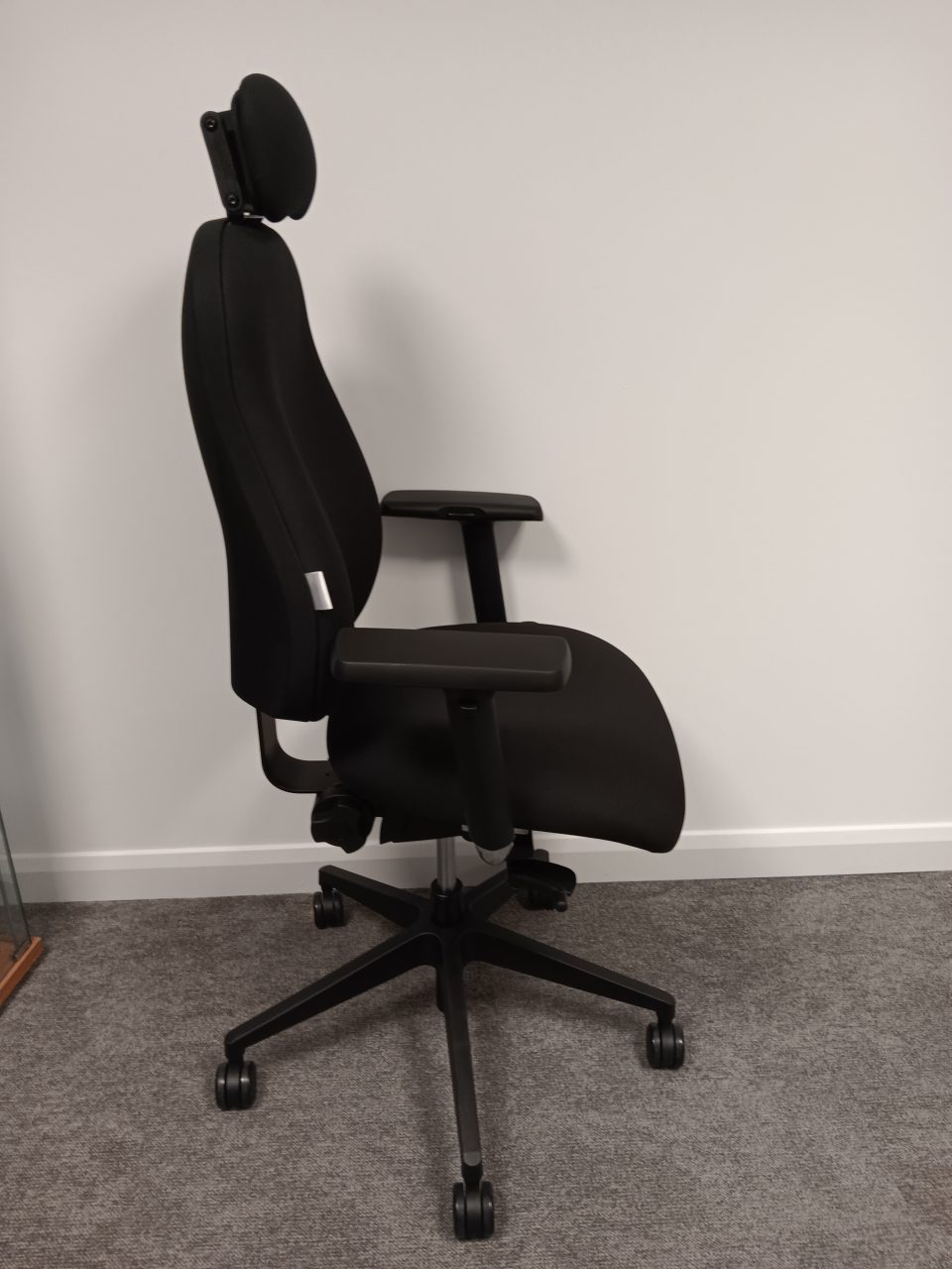 Side view of an RS74 ergonomic office chair in black upholstery with adjustable headrest, contoured backrest, height adjustable armrests, and five star base with castors.