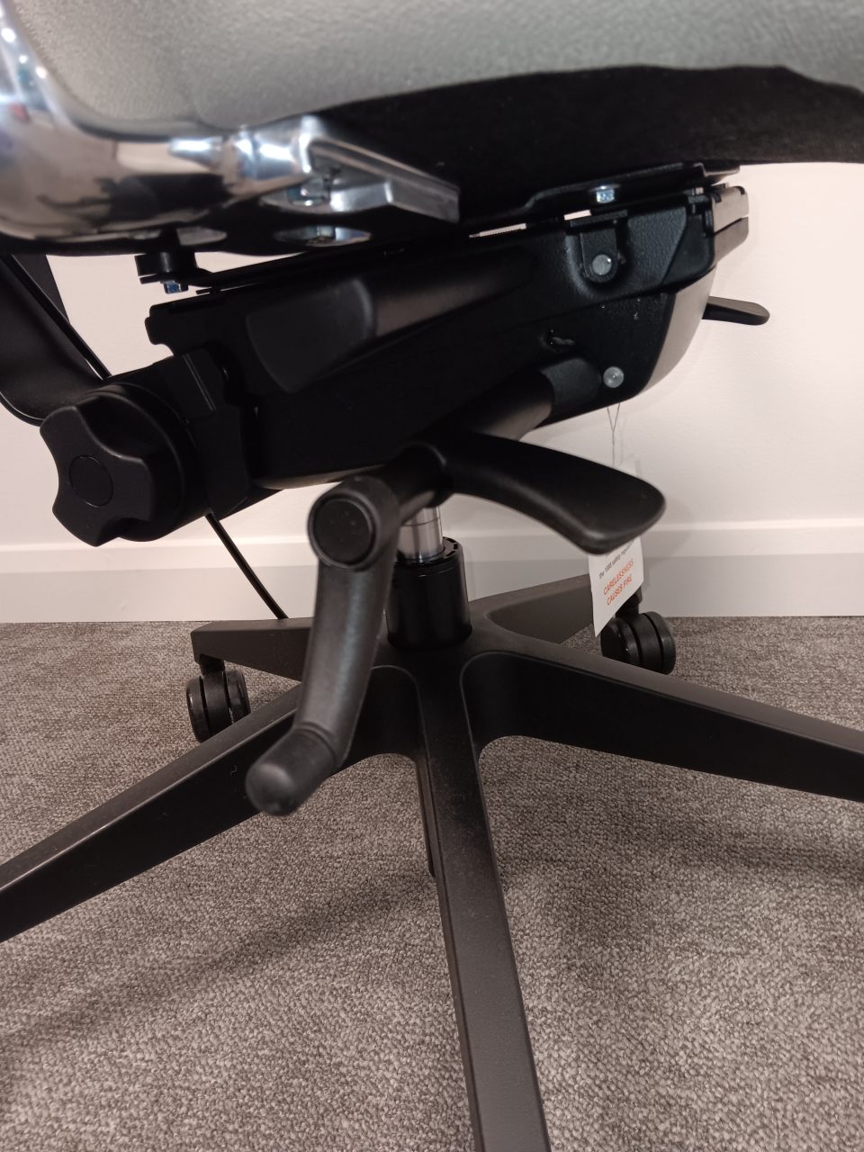 Underside view of an RS74 ergonomic office chair showing adjustment levers, gas lift, tilt mechanism, and five star base with castors.