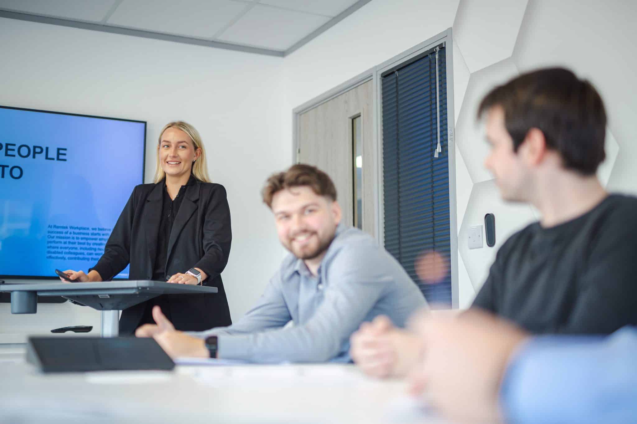 Workplace presentation led by a professional facilitator, with team members seated at a table engaging in discussion during a collaborative office meeting.