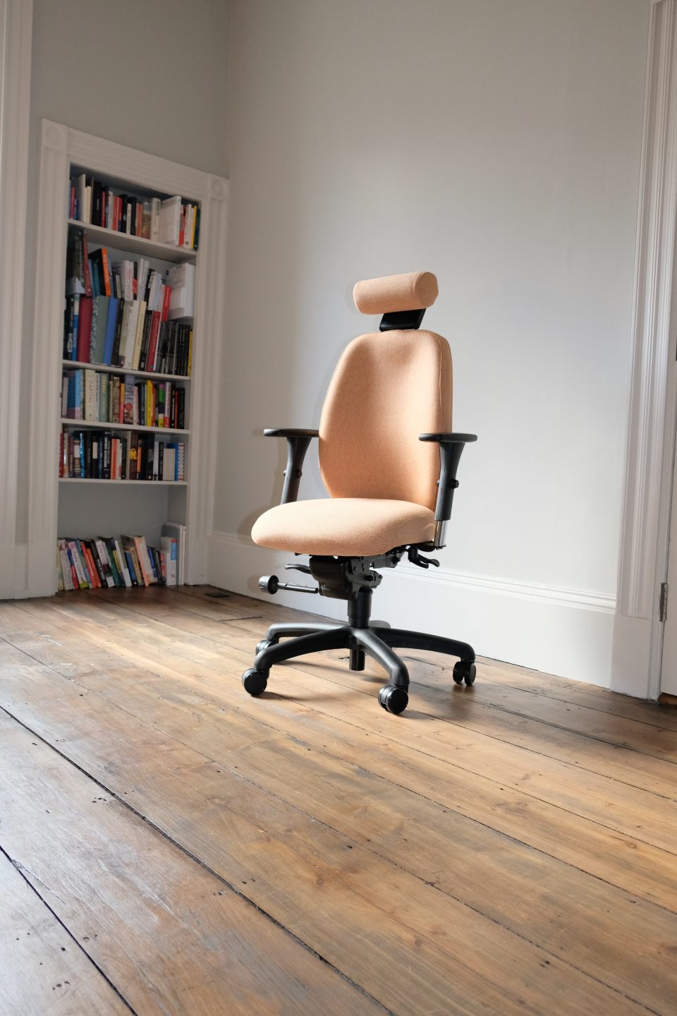 Ergochair Adapt 610 ergonomic chair, upholstered in light orange. image shows chair in a home setting, infront of a white bookcase