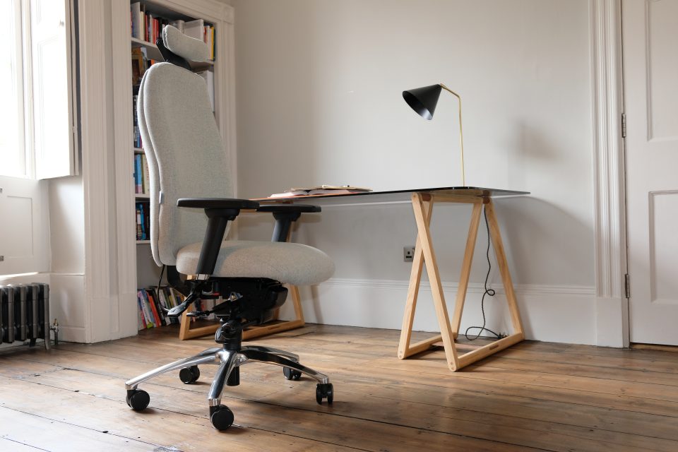 Ergochair Adapt 610 ergonomic chair, upholstered in light grey. image shows chair in a home setting, infront of a desk and white bookcase