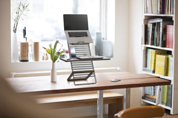 Mousetrapper standfriend in use with a laptop set up. platform is on a wooden desk, with a window showing natural light coming from behind the desk illuminating the workspace