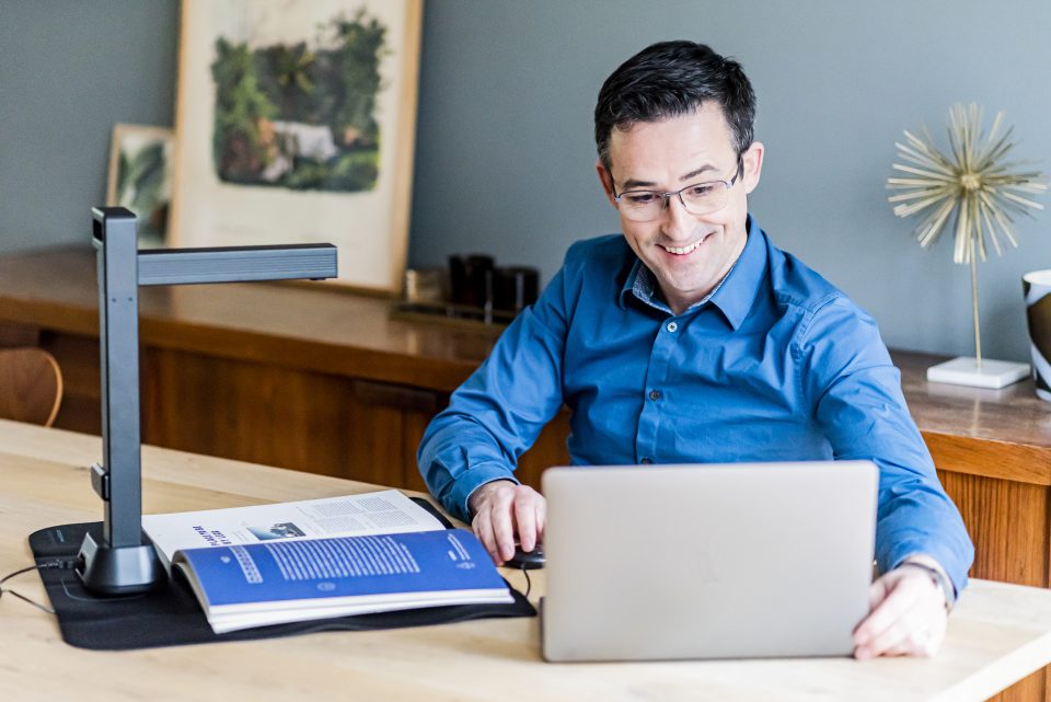 IRIScan Desk 6 Pro in use on desk being used by a blonde man in blue shirt and glasses