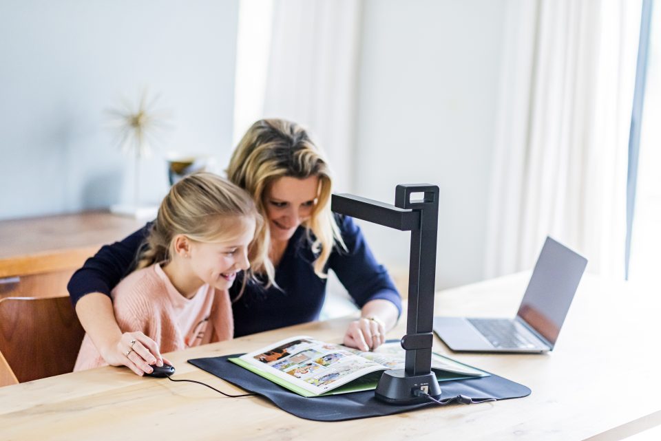 IRIScan Desk 6 Pro in use on desk being used by a blonde woman and child to scan a book