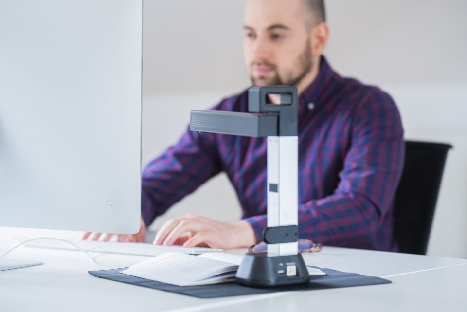 IRIScan Desk 6 set up on a white desk, a man in a purple shirt is scanning adocument