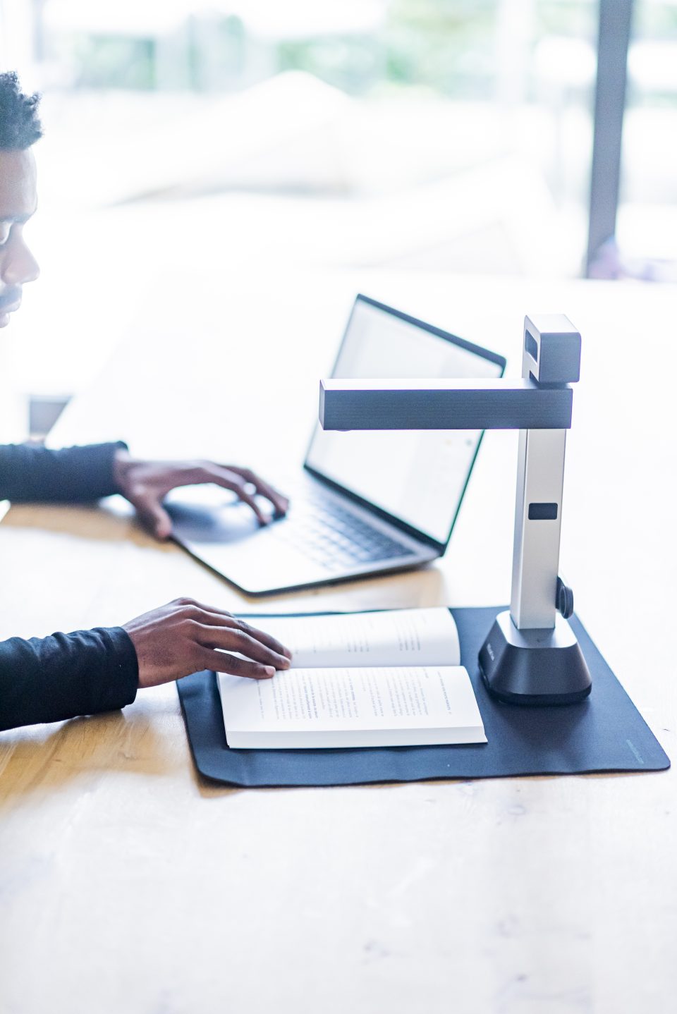 IRIScan Desk 6 set up on a light oak desk, a man in a black turtleneck jumper is scanning a bookscanning