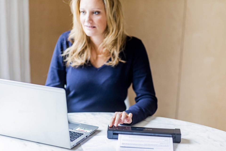 A female office worker using the IRIScan Executive 4 Duplex scanning a page of text. she is focused on her laptop screen