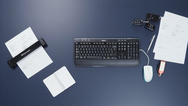 IRIScan Executive 4 device scanning a page of text on a dark blue work surface, with a keyboard, mouse and documents