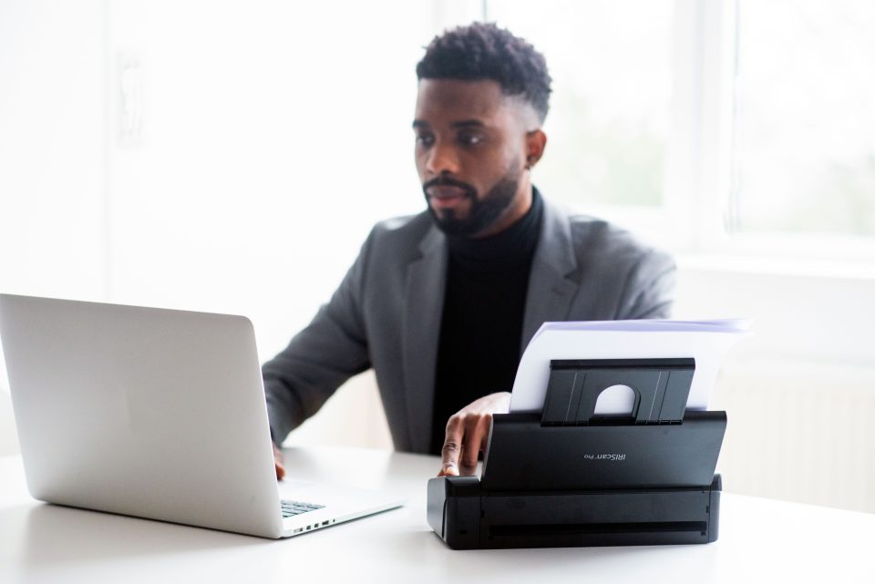 IRIScan Pro 5 in use by man in grey suit and black undershirt. his focus is on his laptop screen