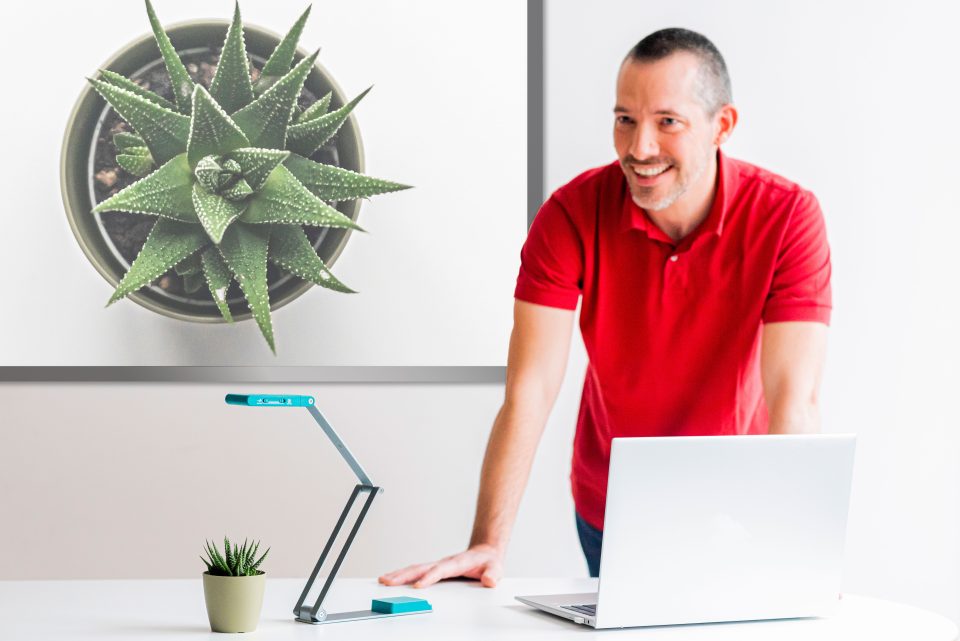 IRIScan Visualizer 7 in use. scanner is magnifying a plant onto a screen behind a teacher in a red polo shirt