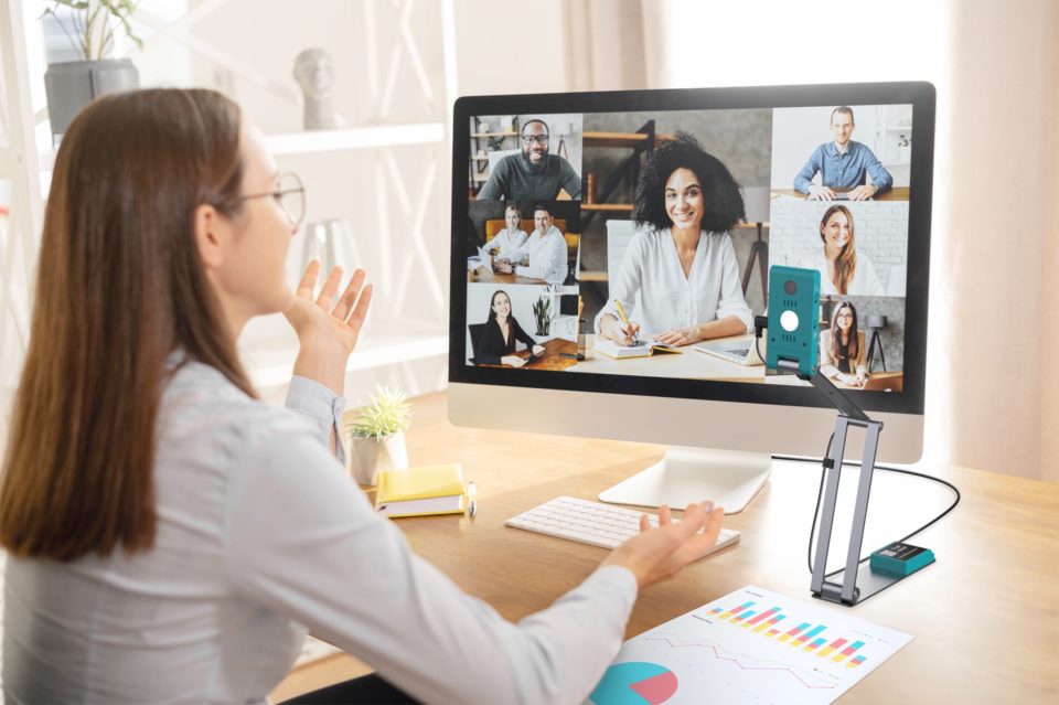 IRIScan Visualizer 7 in use as a webcam, focused on computer user. the monitor has several colleagues in an online meeting