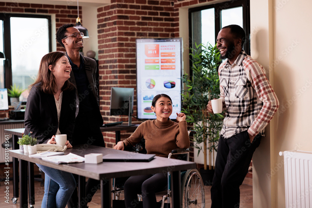 DEI&B inclusive workplace scene showing a diverse team of colleagues, including a wheelchair user, socialising and collaborating together in a modern office, representing accessibility, equity, inclusion, and belonging at work.