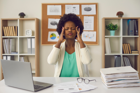Employee experiencing workplace stress while sitting at a desk with paperwork and laptop in an office environment