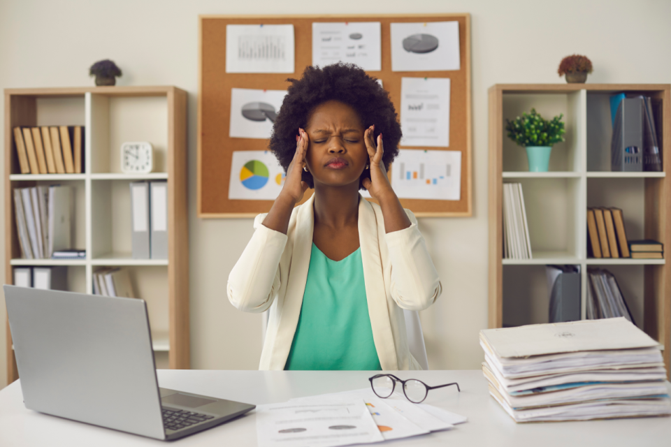 Employee experiencing workplace stress while sitting at a desk with paperwork and laptop in an office environment