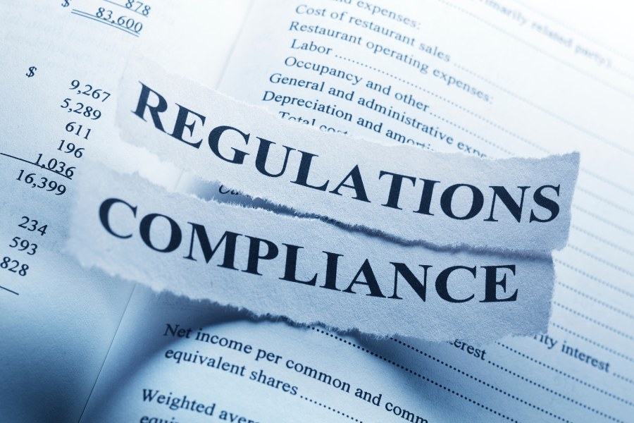 Torn paper strips reading “Regulations” and “Compliance” placed over financial documents, symbolising Display Screen Equipment (DSE) regulatory requirements and workplace compliance.