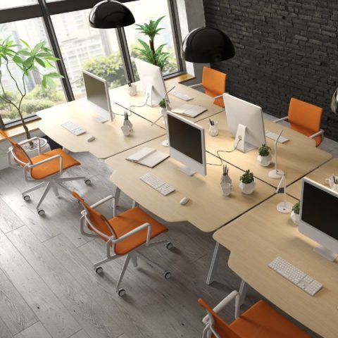 Modern open-plan office workspace with ergonomic desks, orange office chairs, computer monitors, and natural lighting — illustrating proper display screen equipment (DSE) workstation setup.