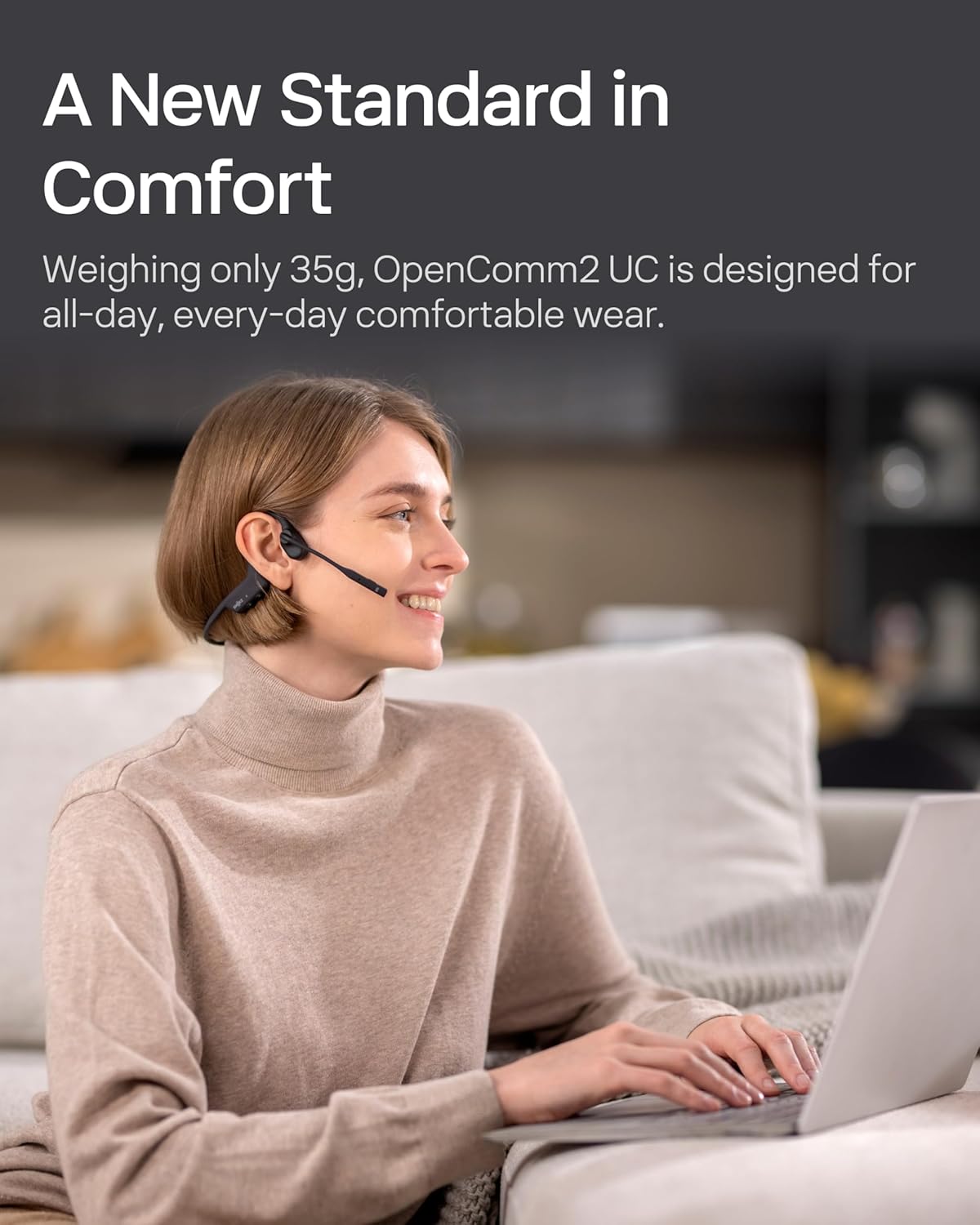 Woman working on a laptop at home wearing the Shokz OpenComm2 UC headset, smiling and appearing comfortable