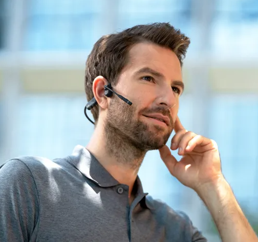 Man in a smart-casual polo shirt smiling while wearing the Shokz OpenComm2 UC headset indoors