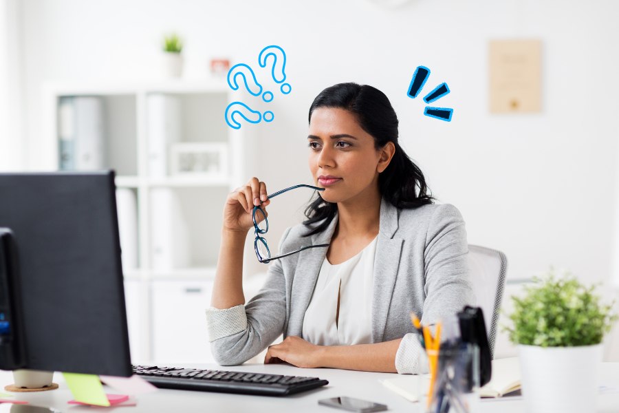 Woman sitting at an office desk looking thoughtfully at her computer, considering whether she needs a wrist support for typing.