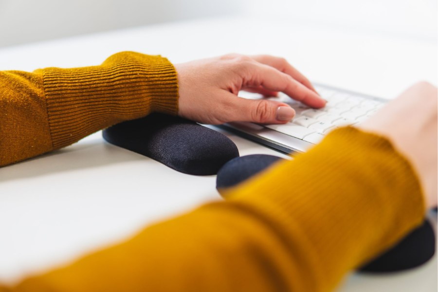 Close-up of a person typing on a keyboard while using black wrist supports to maintain a comfortable wrist position.