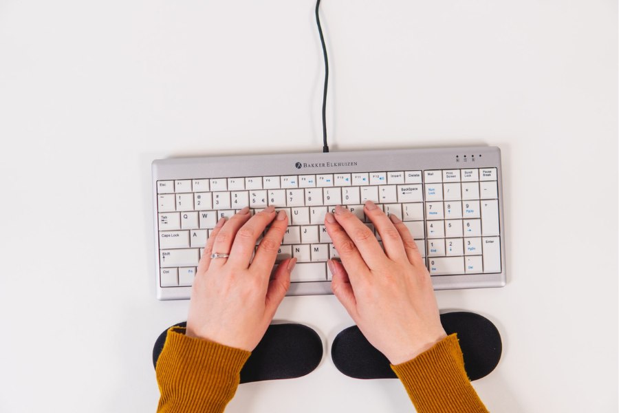 Hands typing on a compact keyboard with a pair of black wrist supports positioned underneath for ergonomic typing comfort.
