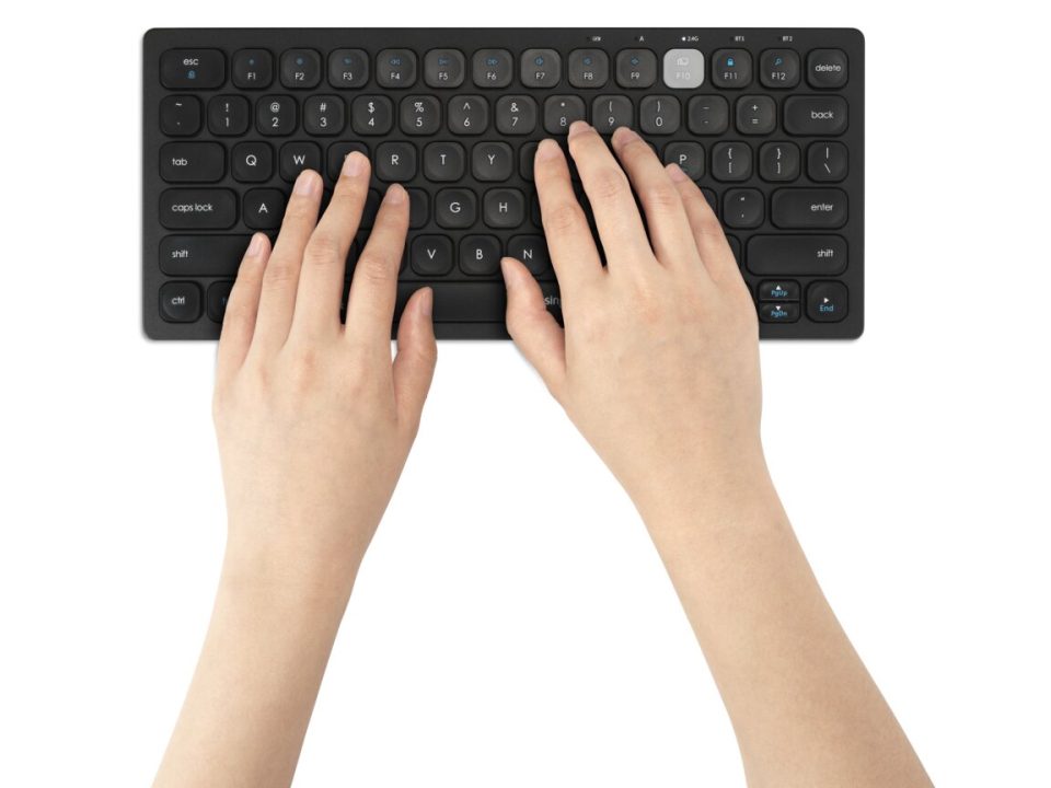 Hands typing on a Kensington compact wireless keyboard with rounded keys on a clean white background.