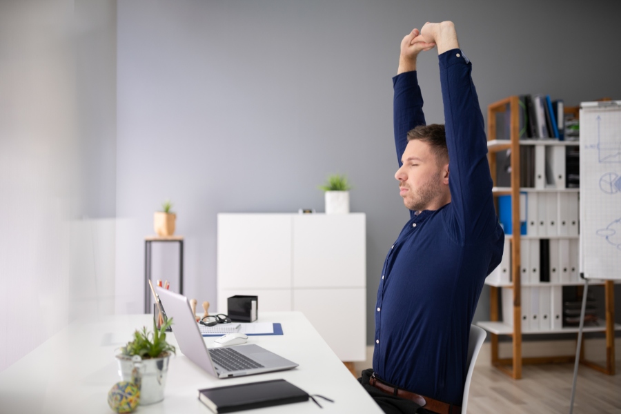 Man sitting at a desk stretching his arms overhead, demonstrating posture improvement during desk work.