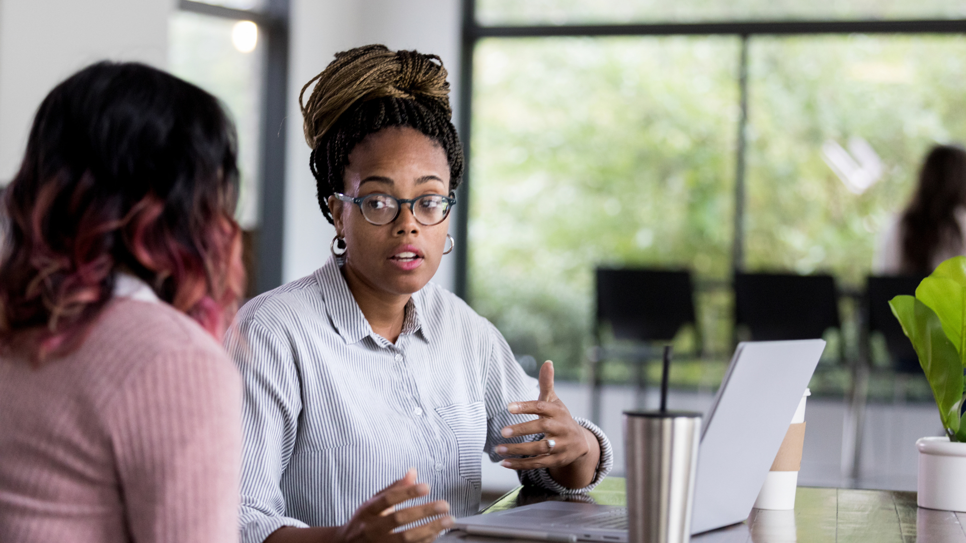 Two women conversing in an office, surrounded by paperwork and a computer.