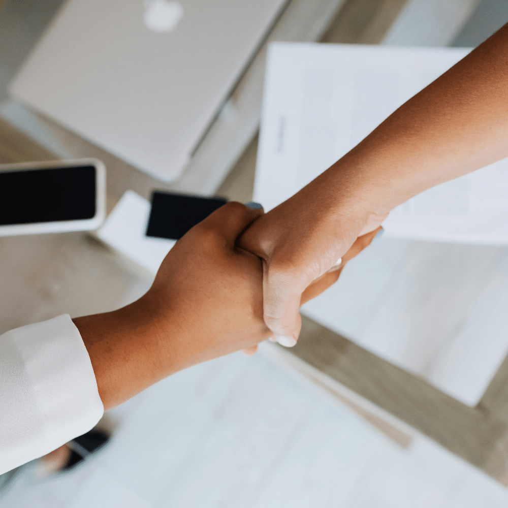Two people shaking hands across a desk in a professional setting.