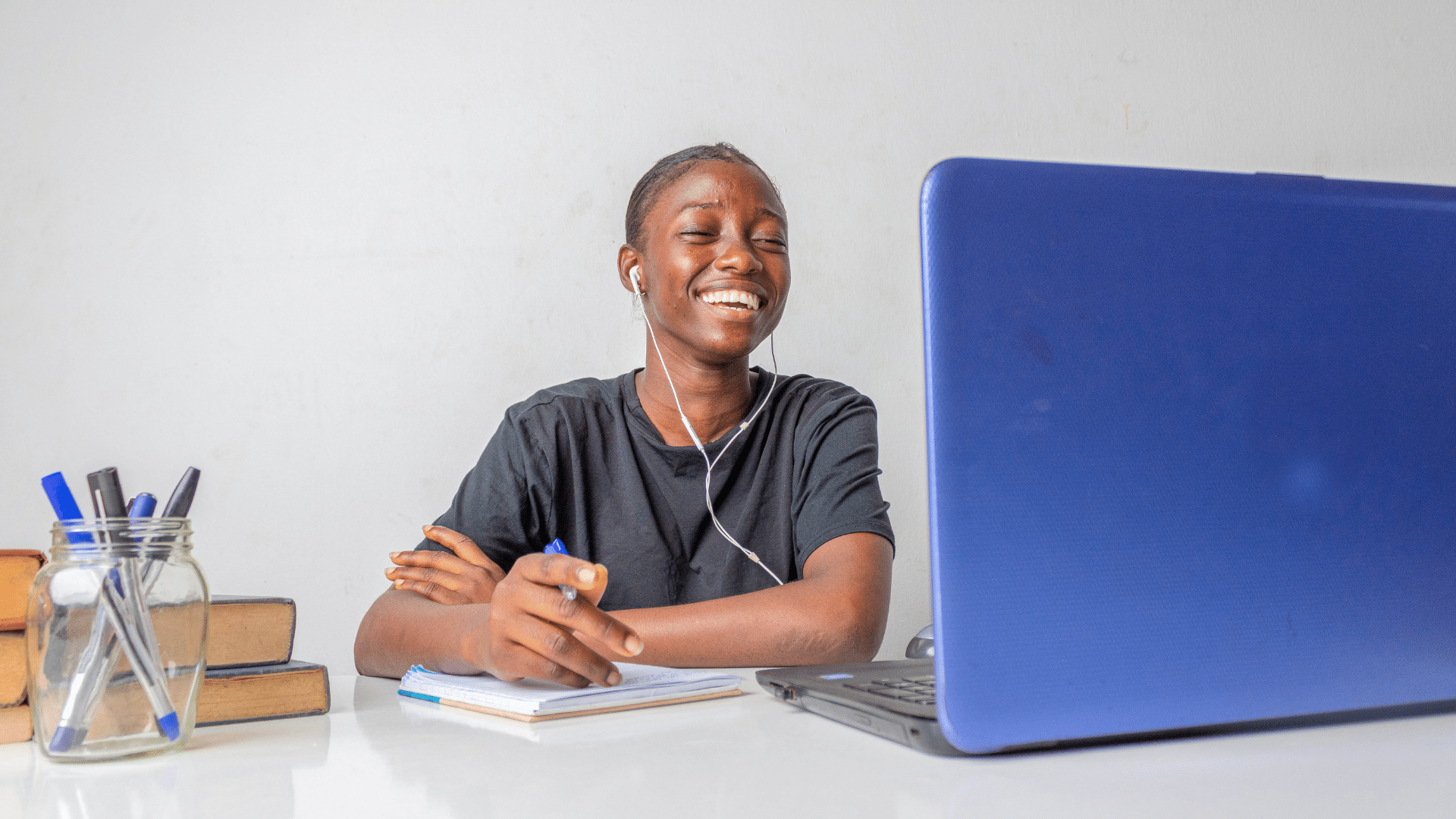 Woman wearing earphones smiling while using a laptop at a desk.