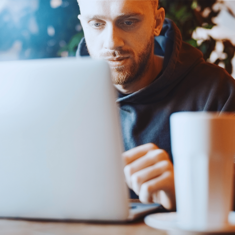 Man concentrating on a laptop at a desk, with a white mug in the foreground.