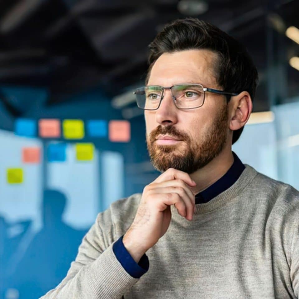 Man thinking thoughtfully with his hand resting on his chin in a modern workplace.