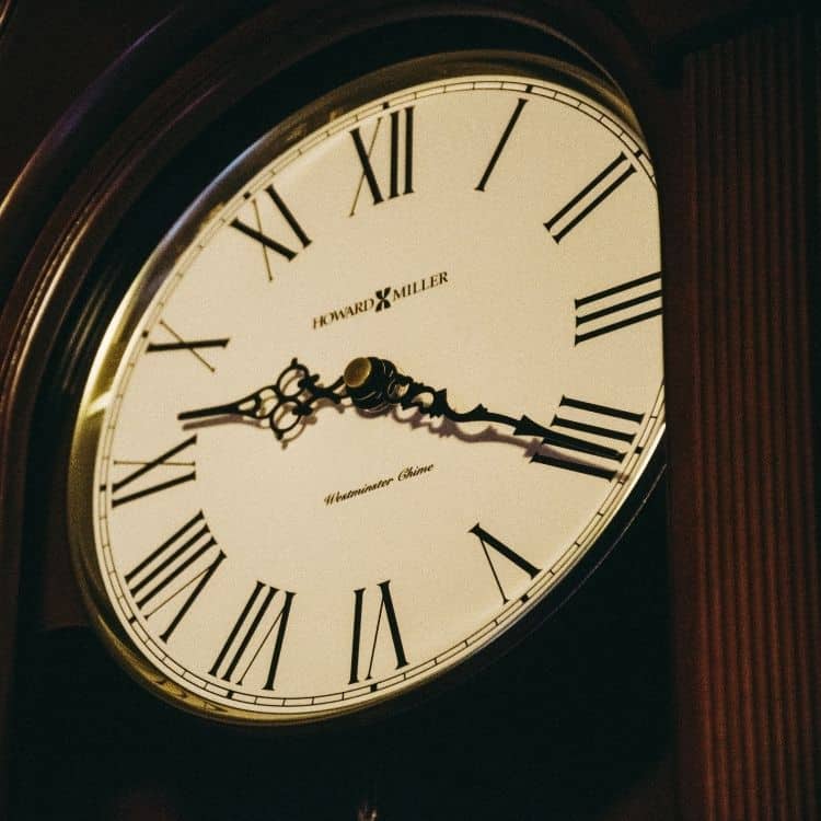 Close up of a traditional analogue clock with Roman numerals and decorative black hands.