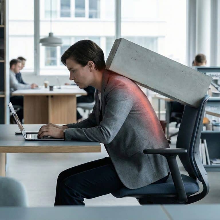 Office worker leaning towards a low laptop screen while seated at a desk.